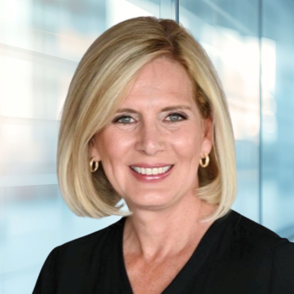 Portrait of a smiling blonde woman in a black top standing by glass walls in an office setting.