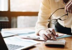 Close up Business woman using calculator and laptop for do math finance on wooden desk in office and business working background, tax, accounting, statistics and analytic research concept