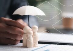 A hand places a small white umbrella over wooden pawn figures on a document, suggesting protection or risk management in business strategy.